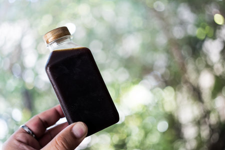 Cold brew coffee bottle on hand against nature background.の写真素材