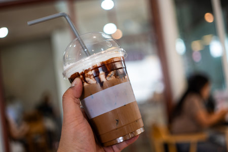 Hand holding iced mocha coffee in plastic glass with blur coffee shop.の写真素材