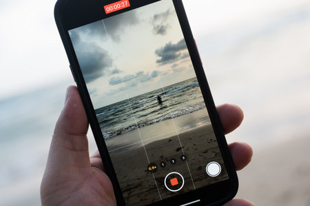 Shooting video with phone. Shooting man walking at the beach, man photographing sea at sunrise with smartphoneの写真素材