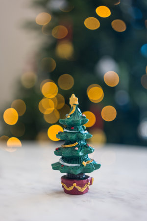 A cute resin mini Christmas tree on the table with a bokeh light Christmas tree backgroundの写真素材
