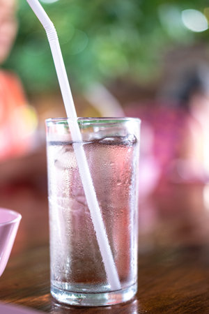 Glass of cold water with ice and straw on tableの写真素材