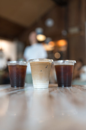 Close up view a glass of ice latte placed on the center between ice black coffee, desk blurred...