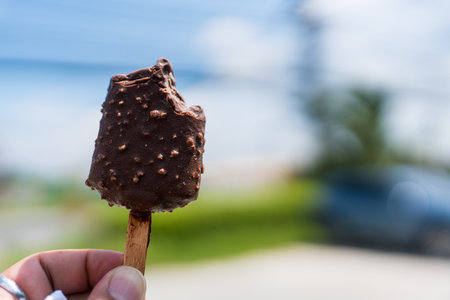 Bitten chocolate ice cream bar with crushed peanut nuts in hand