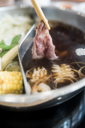 Man holding slice beef out from hot pot shabu shoyu soup base by chopsticks with steam.の写真素材
