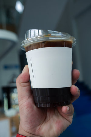 Hand holding ice coffee in plastic glass with white paper sleeve cup