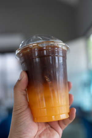 Iced americano black coffee and layer of orange juice on handの写真素材