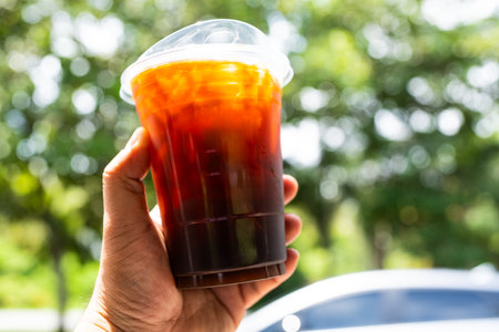 Hand of man holding a take out iced black coffee with nature bokeh backgroundの写真素材