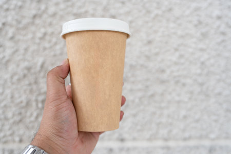 Hand holding a brown paper cup with white lid of hot coffeeの写真素材