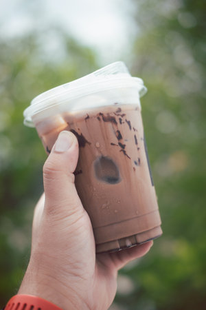 Man hand holding cold mocha coffee on a green background in the morning light.の写真素材