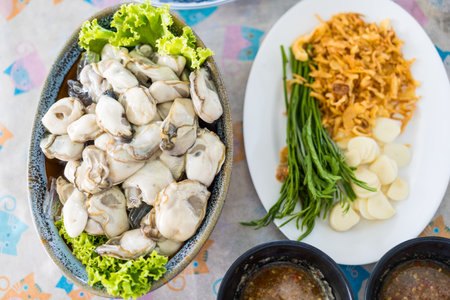 Fresh Thai style oysters soaked with ice you can eating together with spicy seafood sauce, fried shallots, fresh garlic and acacia shootsの写真素材
