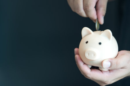 The person putting coin into piggy bank to save money and invest for growth in future. Save money for future. Person is putting a coin into a piggy bank with copy spaceの写真素材
