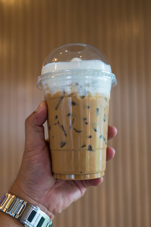 Iced coffee latte with milk cream topping on man hand. Summer refreshment drink concept