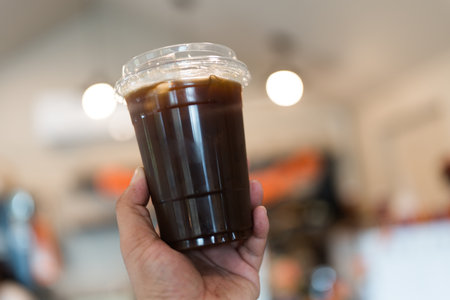 Closeup shot of man holding a plastic glass of iced black coffee or americanoの写真素材