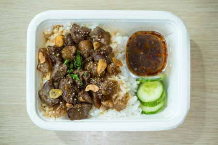Lunch paper box with Thai beef on rice served with sauce and cucumber slice. Top viewの写真素材