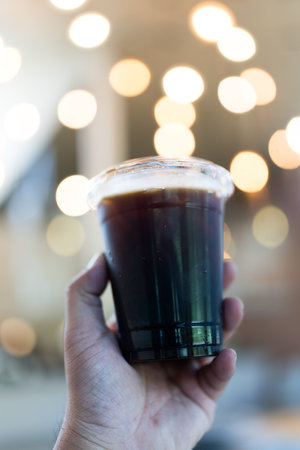 Iced black coffee americano in take away cup on hand with bokeh background
