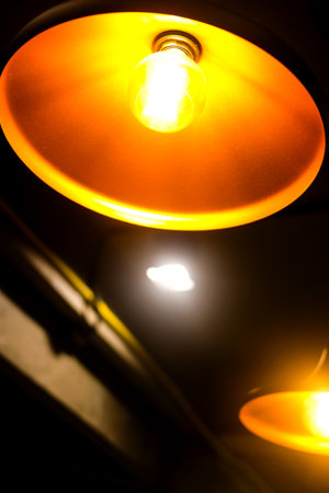 A glowing light bulb hangs from a chain against, radiating warm orange light.の写真素材