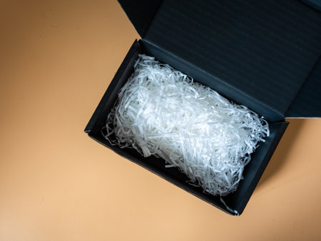 Black cardboard box with white shredded paper safety fragile product delivery shipment. Top view