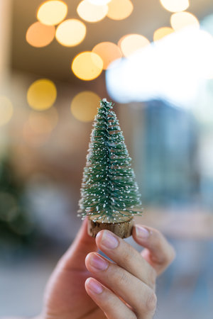 Hand holding a cute resin mini Christmas tree with bokeh lightの写真素材