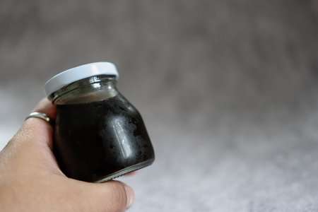 Close up hand holding take away glass bottle of black coffeeの写真素材