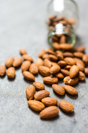 A glass jar spills fresh almonds on a gray surface. Close upの写真素材