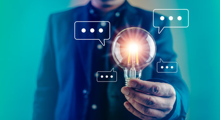 A Businessman is holding a light bulb and many popup of talking bubble. Symbolizing the thinking and new ideaの写真素材