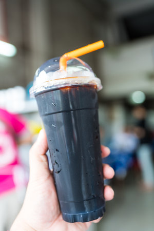 Thai style iced black coffee in plastic glass on hand