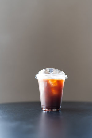 Iced americano coffee in a disposable glass on table. Cold summer drink on grey background with copy space.の写真素材