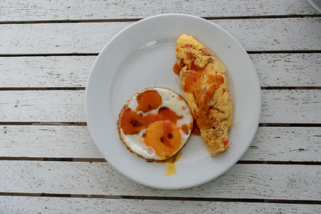 Fried eggs and omelets with chili sauce on a plate, tasty breakfast serving