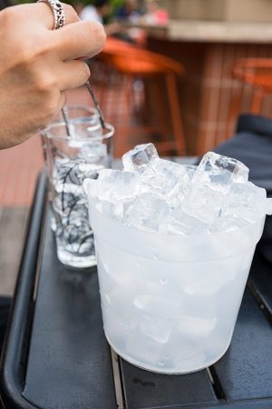 Man use stainless steel tongs keep ice in to glass for drinkの写真素材