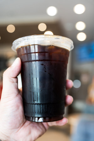 Hand of man holding a take out iced black coffee at coffee shop,の写真素材