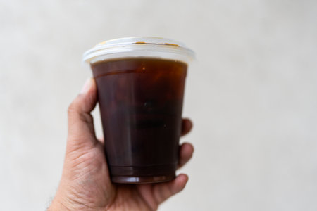 Hand holding a plastic cup of americano coffee take away, black coffee without sugar