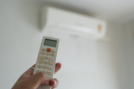Hand holding remote control with blur air conditioner background. Energy saving sustainable lifestyleの写真素材