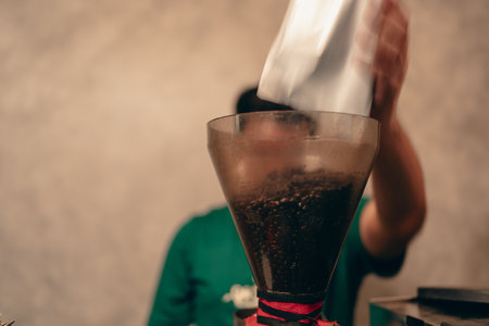 Barista pours coffee beans into the coffee machine tank for grinding standing behind counter. Close upの写真素材