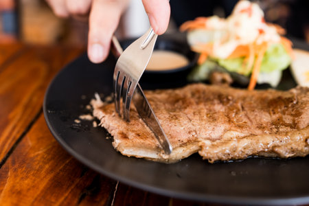 Close up hand eating delicious grilled steak on dish in restaurantの写真素材