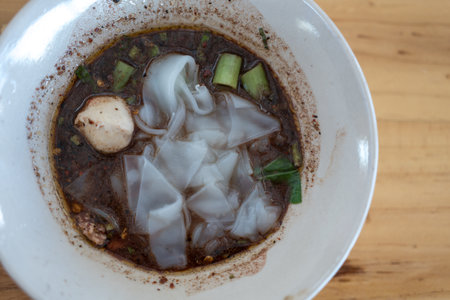 Delicious Thai boat yellow noodle soup with meatball and morning glory in a small bowl on wood tableの写真素材