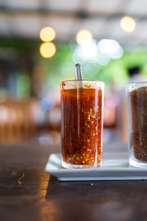 Spicy pickled sliced chili in vinegar in a tall glass. Thai condiments on the table