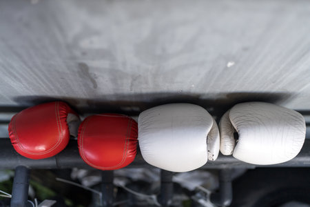 Two red and white boxing mitts hanging in an indoor gym, symbolizing competitive fighting and athletic confrontationの写真素材