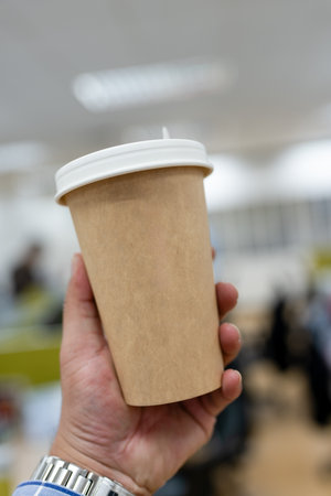 Brown paper coffee cup with a white paper lid on man hand at officeの写真素材