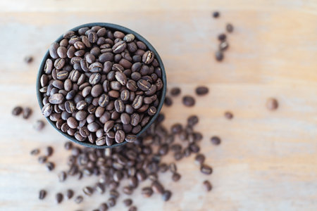 Roasted coffee beans in dark bowl on wood tableの写真素材