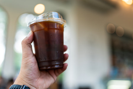Hand holding a plastic cup of iced americano coffee take awayの写真素材