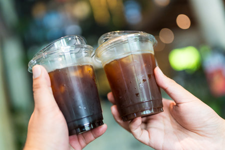 Iced Americano coffee cheers with friends. Two men joyfully clinking glasses filled with refreshing...