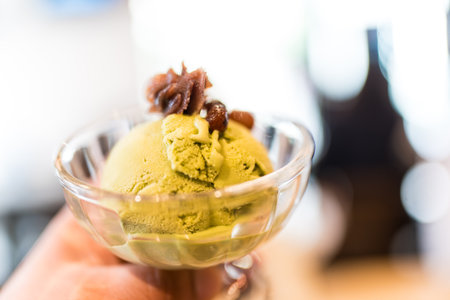Matcha green tea ice cream is elegantly presented in a glass bowl, generously topped with red bean...