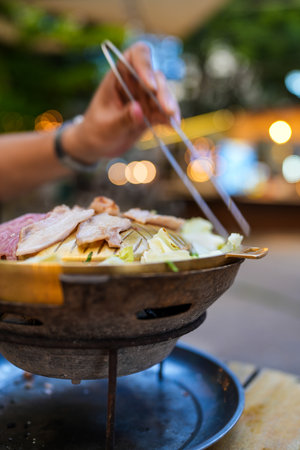Unrecognizable man is enjoying cooking and eating Moo Ka Ta in outdoor restaurantの写真素材