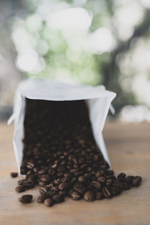White paper coffee bag packaging on a wooden surface alongside scattered coffee beansの写真素材