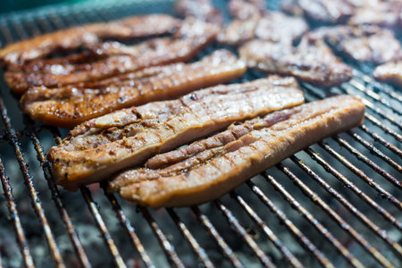 Pieces of Thai pork grilled on a bbq stove outdoor at night time