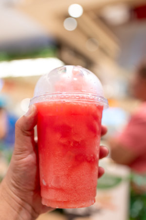 Hand holding watermelon smoothie drink in plastic cup