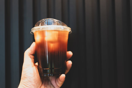 Close up of a hand holding an Americano or black coffee in plastic glass.