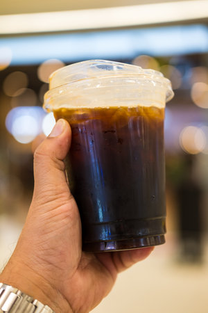 Hand holding a take away plastic cup of americano coffeeの写真素材