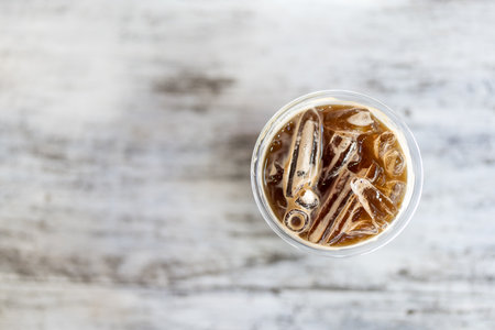 A coffee cup with an iced beverage is placed on a minimal white wood background. Directly above shotの写真素材