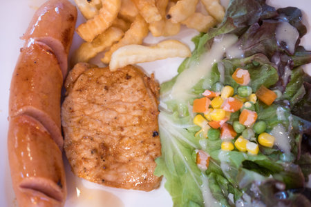 Pork steak and hot dog served with salad and french fries. Top viewの写真素材
